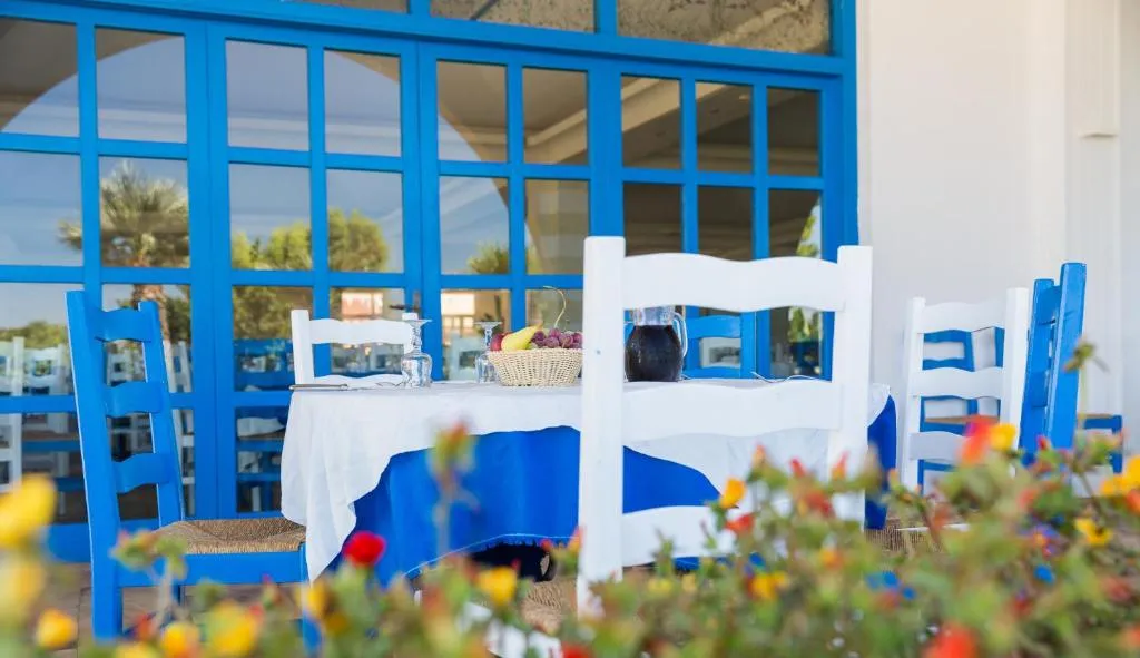 Tavolo esterno del ristorante con sedie blu e bianche tra i fiori colorati